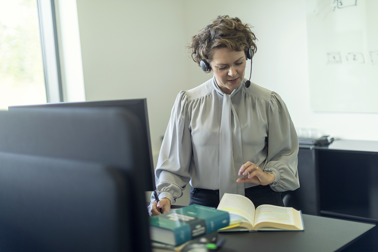 kvinde på arbejde der kigger i bog ved skrivebord